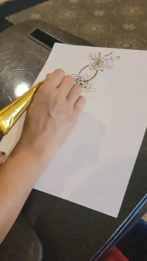 Jahnavi practicing a henna design on paper with a gold cone on the morning of the festival